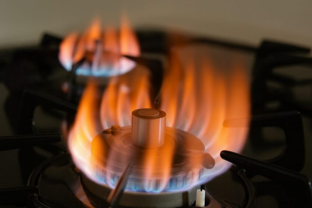 ガスコンロの炎が赤く燃えている様子を横から撮影した写真。青い炎に赤火が混ざり、燃焼の異常を示すような印象的な光景。