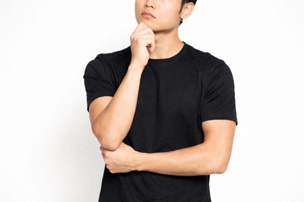腕を組みながら顎に手を当て、考え込むポーズをしている黒Tシャツの男性の横長イメージ画像