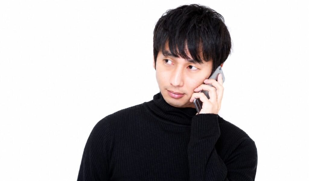 黒いタートルネックを着た男性がスマートフォンで通話している横長のポートレート写真