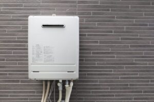 タイル調の外壁に壁掛け設置された屋外用ガス給湯器と、下部に接続された給水・給湯配管が見える設置状態の様子