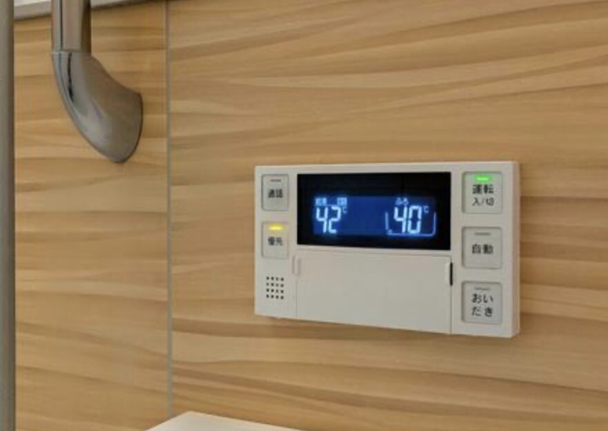 浴室の壁に設置された給湯器リモコンに、設定温度と湯温がデジタル表示されている操作パネルの様子
