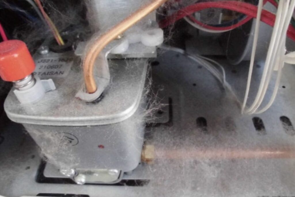 石油ストーブ内部に設置された電磁ポンプ周辺の様子。銅製の燃料配管や電線が接続され、内部にホコリやクモの巣が付着している状態が確認できる。