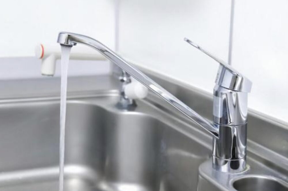 キッチンのシンクに設置された混合水栓から水が流れており、レバー操作部と吐水口の形状が確認できる使用中の状態