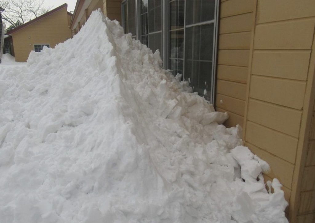 建物外壁の低い位置に設置されたストーブの排気トップが、吹き溜まりによる積雪で埋まり、排気口周辺が雪に覆われている状態。