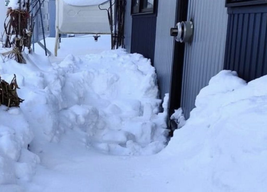 住宅外壁に設置されたFF式ストーブの排気トップ周辺に大量の雪が積もり、通路状に除雪されているものの、排気口の位置が積雪に囲まれている屋外の様子。