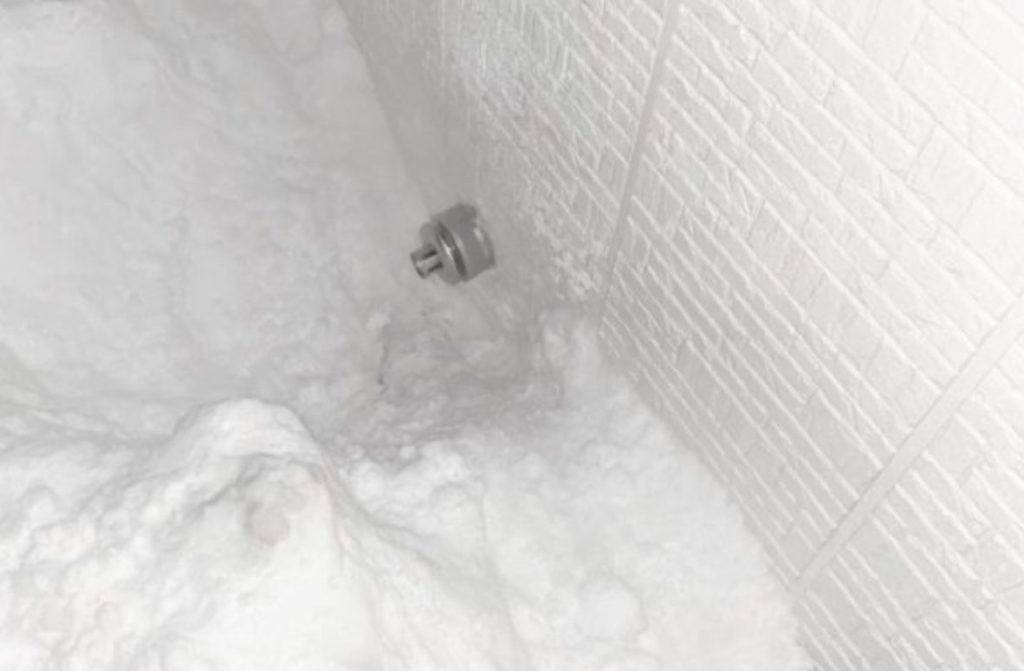 建物外壁の低い位置に設置されたストーブの排気トップが、吹き溜まりによる積雪で埋まり、排気口周辺が雪に覆われている状態。