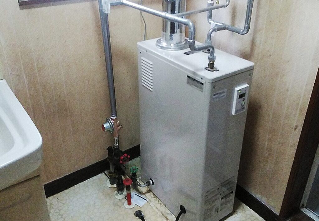 FF式石油給湯器が洗面所の床置きスペースに設置され、排気筒と給水・給湯配管が接続されている様子